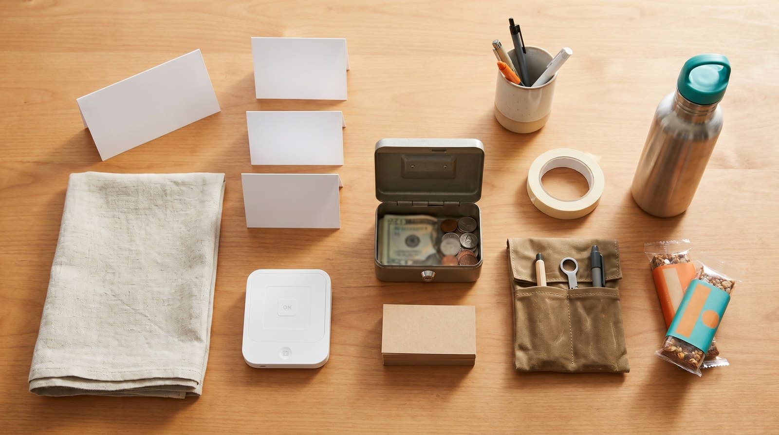 An overhead flat-lay of craft fair vendor essentials: tablecloth, price signs, card reader, cash float, business cards, and supplies.