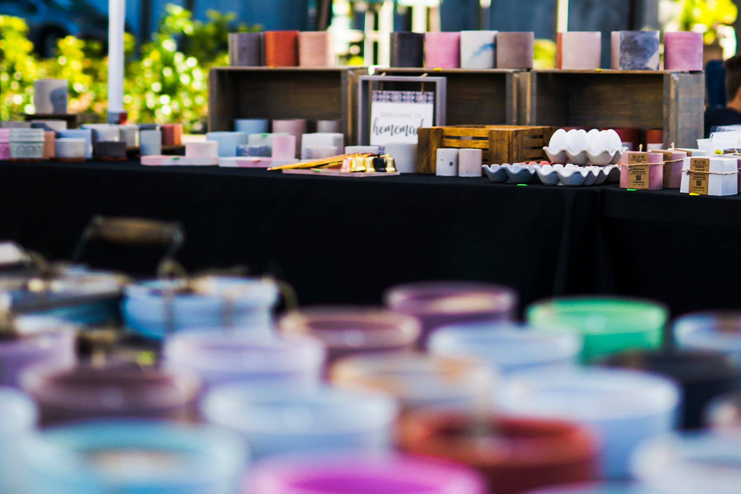 A candle and soap vendor's booth — rows of glass jar candles and stacked soap bars on warm wood shelving in golden-hour light.