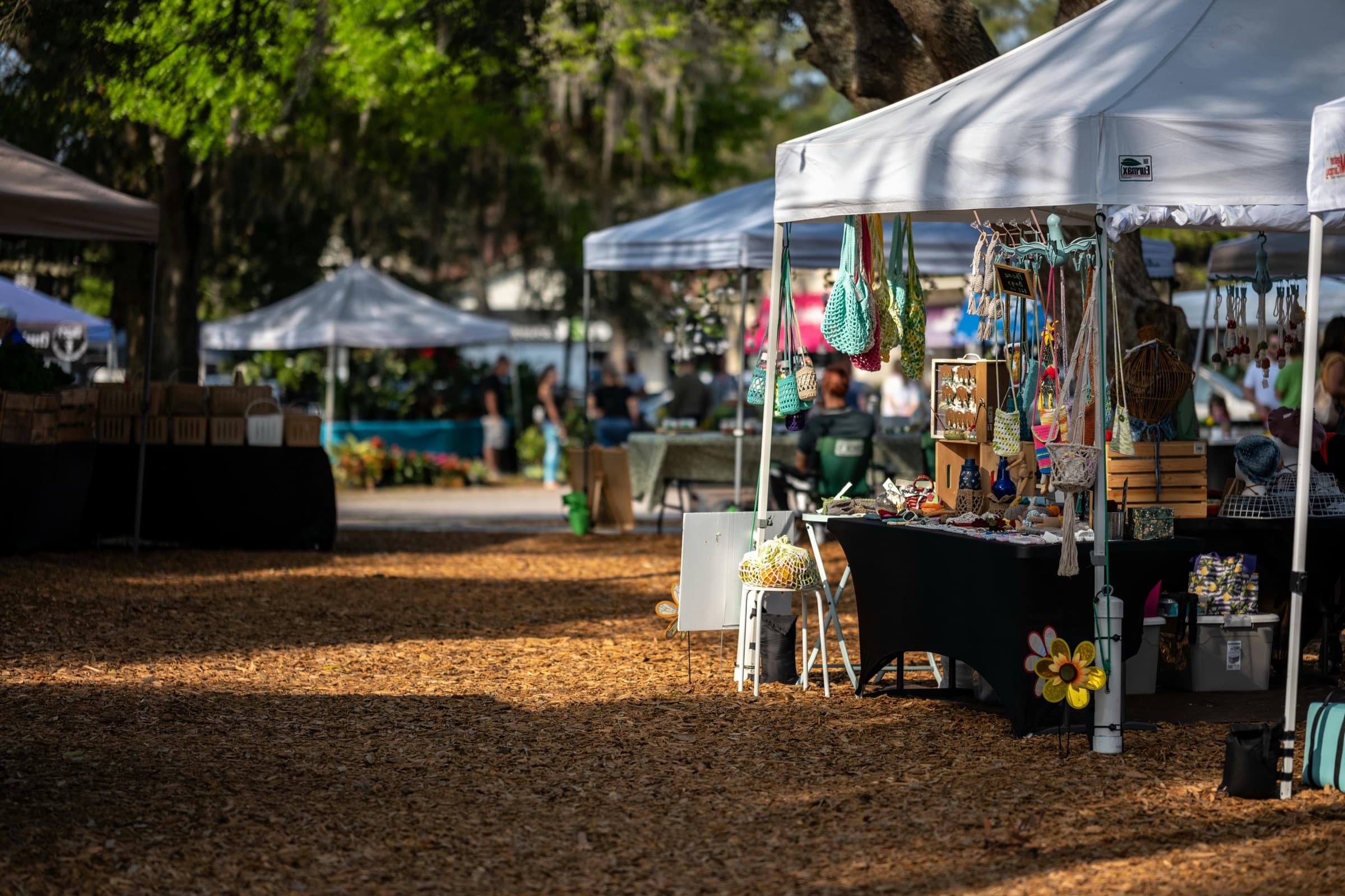 A row of craft fair booths at golden hour — jewelry, ceramics, candles, and apparel vendors setting up for the day.