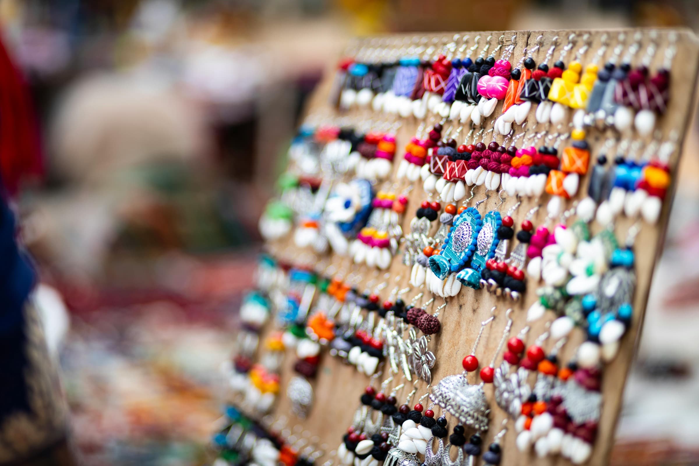 A jewelry vendor's booth at golden hour — earring cards, ring stands, and necklace busts arranged on a linen-covered table.